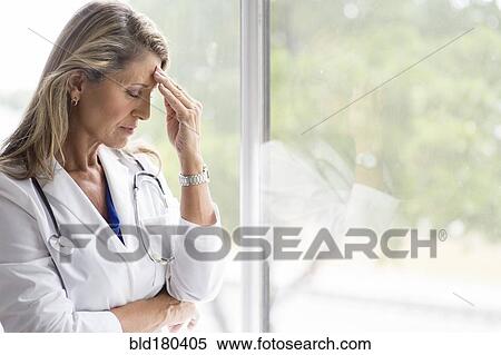 Caucasian doctor rubbing forehead at window View Large Photo Image Stock Photography - Caucasian doctor rubbing forehead at window. Fotosearch