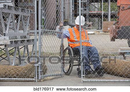 Stock Photo - Caucasian engineer in wheelchair opening construction site gate. Fotosearch