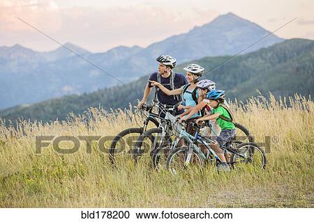 Stock Image - Caucasian family riding mountain bikes in field. Fotosearch