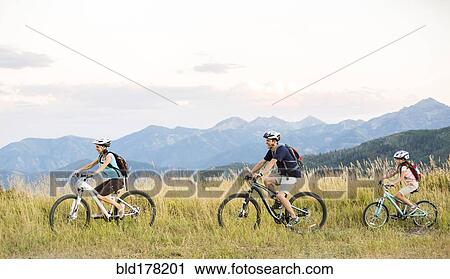Stock Image - Caucasian family riding mountain bikes in field. Fotosearch