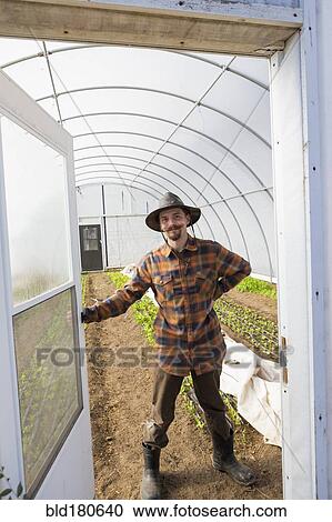 Stock Image - Caucasian farmer opening greenhouse door. Fotosearch