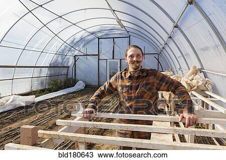 Stock Image - Caucasian farmer standing in greenhouse. Fotosearch