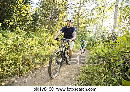 Stock Image - Caucasian father and children riding mountain bikes. Fotosearch