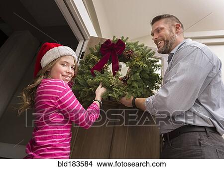 Picture - Caucasian father and daughter hanging Christmas wreath. Fotosearch