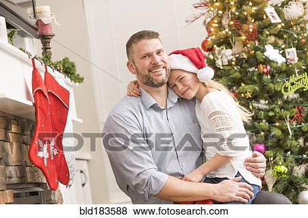 Stock Photo - Caucasian father and daughter hugging near Christmas tree. Fotosearch