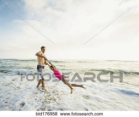 Stock Photo - Caucasian father and daughter playing in waves on beach. Fotosearch