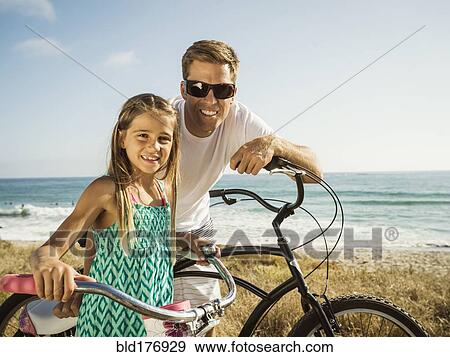 Stock Photo - Caucasian father and daughter riding bicycles on beach. Fotosearch