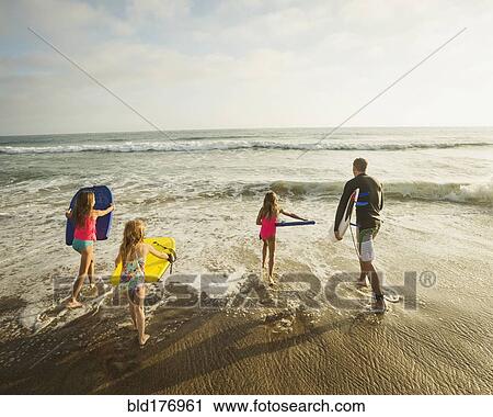 Stock Image - Caucasian father and daughters playing in waves on beach. Fotosearch