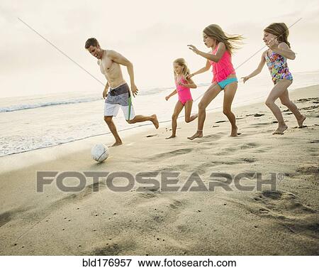 Stock Photo - Caucasian father and daughters playing soccer on beach. Fotosearch