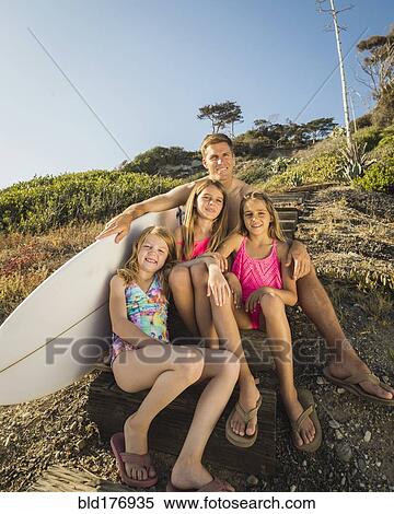 Stock Photography - Caucasian father and daughters sitting on hillside. Fotosearch