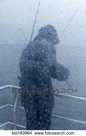 Picture - Caucasian fisherman standing on rainy boat deck. Fotosearch