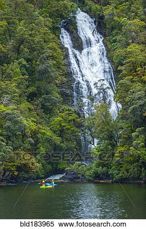 Stock Photography - Caucasian friends paddling kayak under remote waterfall. Fotosearch