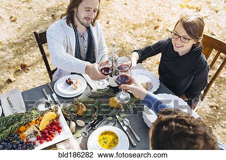 Stock Image - Caucasian friends toasting with wine at outdoor table. Fotosearch