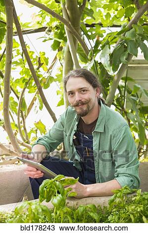 Stock Image - Caucasian gardener using digital tablet in greenhouse. Fotosearch