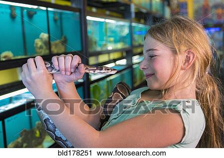 Stock Image - Caucasian girl admiring snake in pet store. Fotosearch