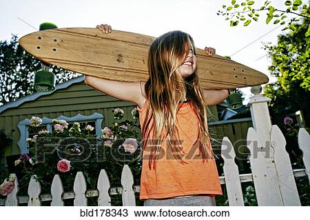 Stock Image - Caucasian girl carrying skateboard outdoors. Fotosearch