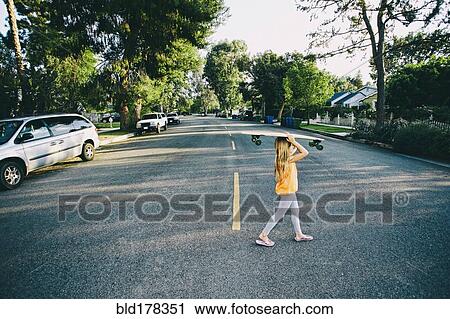 Stock Image - Caucasian girl crossing suburban street. Fotosearch