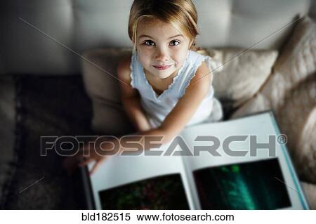 Stock Photography - Caucasian girl reading book on sofa. Fotosearch