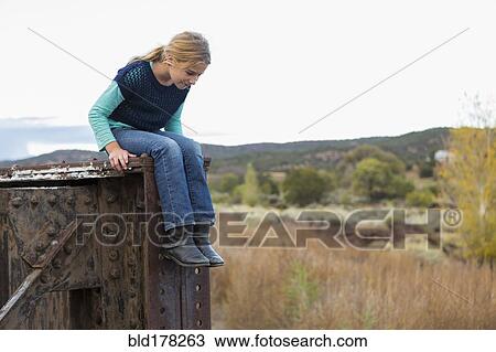 Stock Image - Caucasian girl sitting on structure outdoors. Fotosearch