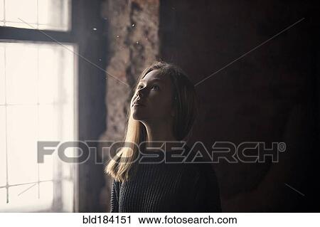 Stock Image - Caucasian girl standing at window. Fotosearch