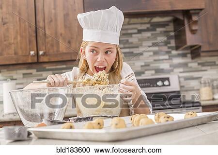Stock Image - Caucasian girl tasting cookie dough in kitchen. Fotosearch