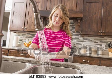 Stock Image - Caucasian girl washing hands in kitchen sink. Fotosearch