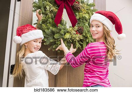 Stock Photograph - Caucasian girls hanging Christmas wreath. Fotosearch