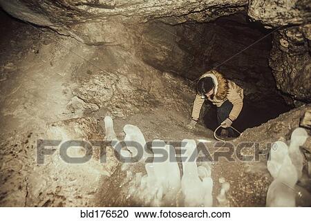 Stock Image - Caucasian hiker climbing in cave. Fotosearch