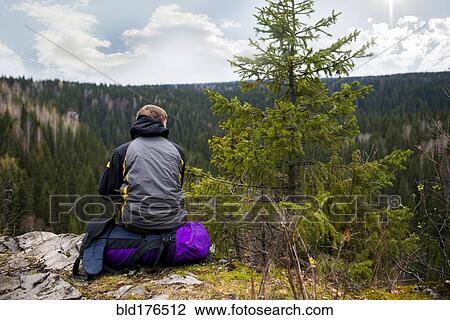 Stock Image - Caucasian hiker sitting on remote hilltop. Fotosearch