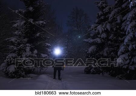 Stock Image - Caucasian hiker wearing headlamp in snowy forest. Fotosearch
