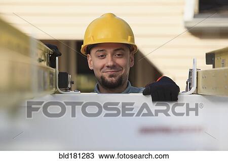 Stock Image - Caucasian installer pulling ladder from truck roof. Fotosearch