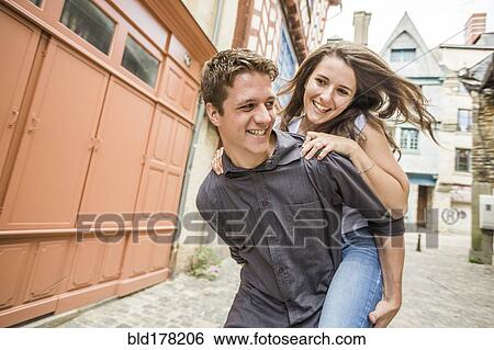 Stock Photograph - Caucasian man carrying girlfriend piggyback in village. Fotosearch