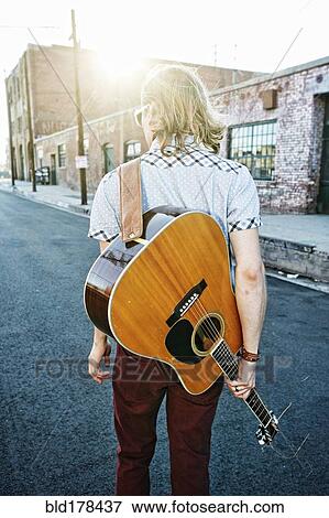 Stock Photo - Caucasian man carrying guitar outdoors. Fotosearch