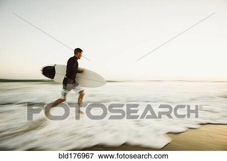 Stock Photo - Caucasian man carrying surfboard on beach. Fotosearch