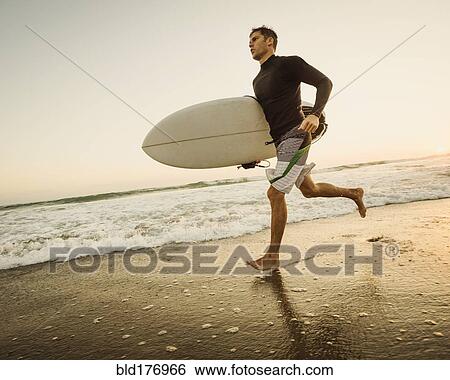 Stock Photograph - Caucasian man carrying surfboard on beach. Fotosearch