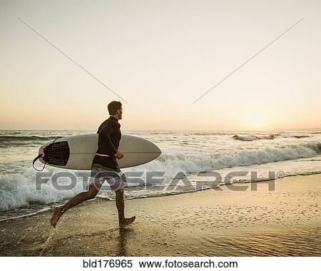 Stock Photography - Caucasian man carrying surfboard on beach. Fotosearch