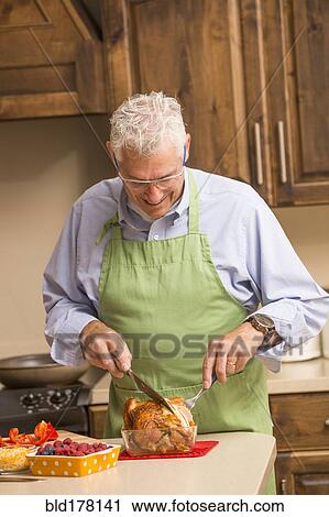 Stock Image - Caucasian man carving chicken in kitchen. Fotosearch