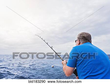 Stock Image - Caucasian man fishing in ocean. Fotosearch