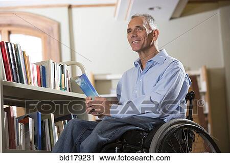 Stock Image - Caucasian man holding book in library. Fotosearch