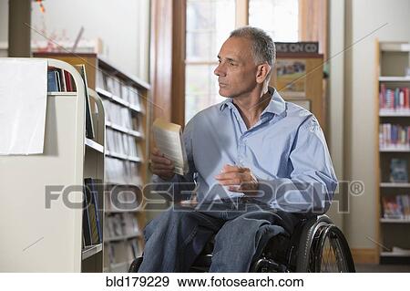 Stock Photo - Caucasian man holding book in library. Fotosearch
