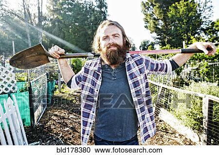 Stock Image - Caucasian man holding shovel in garden. Fotosearch