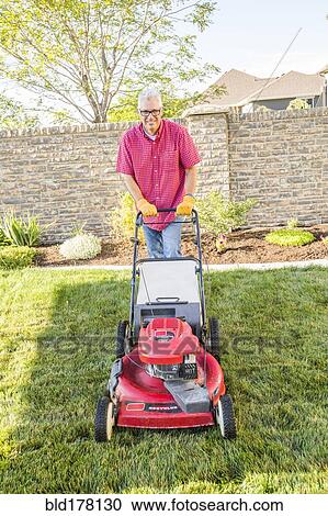 Stock Image - Caucasian man mowing lawn in backyard. Fotosearch
