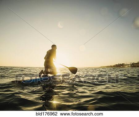 Stock Image - Caucasian man on paddle board in ocean. Fotosearch