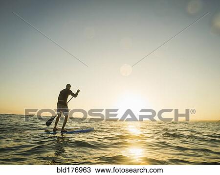 Stock Image - Caucasian man on paddle board in ocean. Fotosearch