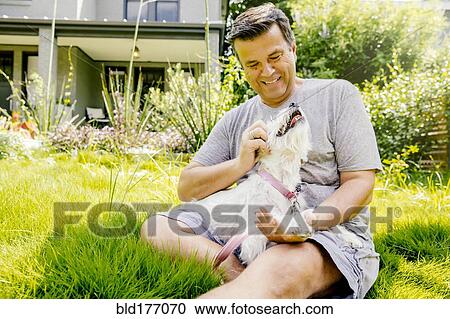 Stock Image - Caucasian man petting dog in grass. Fotosearch
