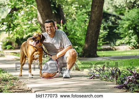 Stock Image - Caucasian man petting dog on sidewalk. Fotosearch