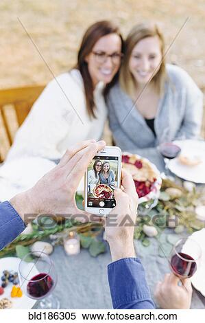 Stock Photography - Caucasian man photographing friends at outdoor table. Fotosearch