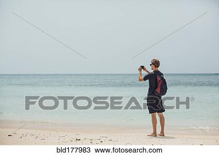 Stock Image - Caucasian man photographing seascape. Fotosearch