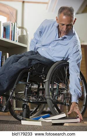Stock Image - Caucasian man picking up books in library. Fotosearch
