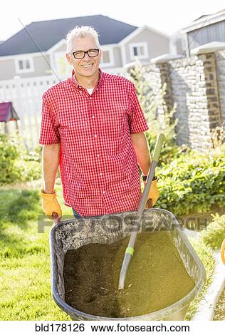 Stock Photograph - Caucasian man pushing wheelbarrow of dirt. Fotosearch
